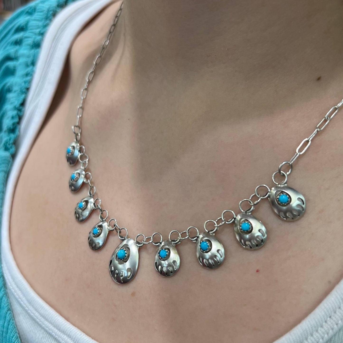 A silver turquoise necklace handmade with nine silver bear paws set with round turquoise stones.