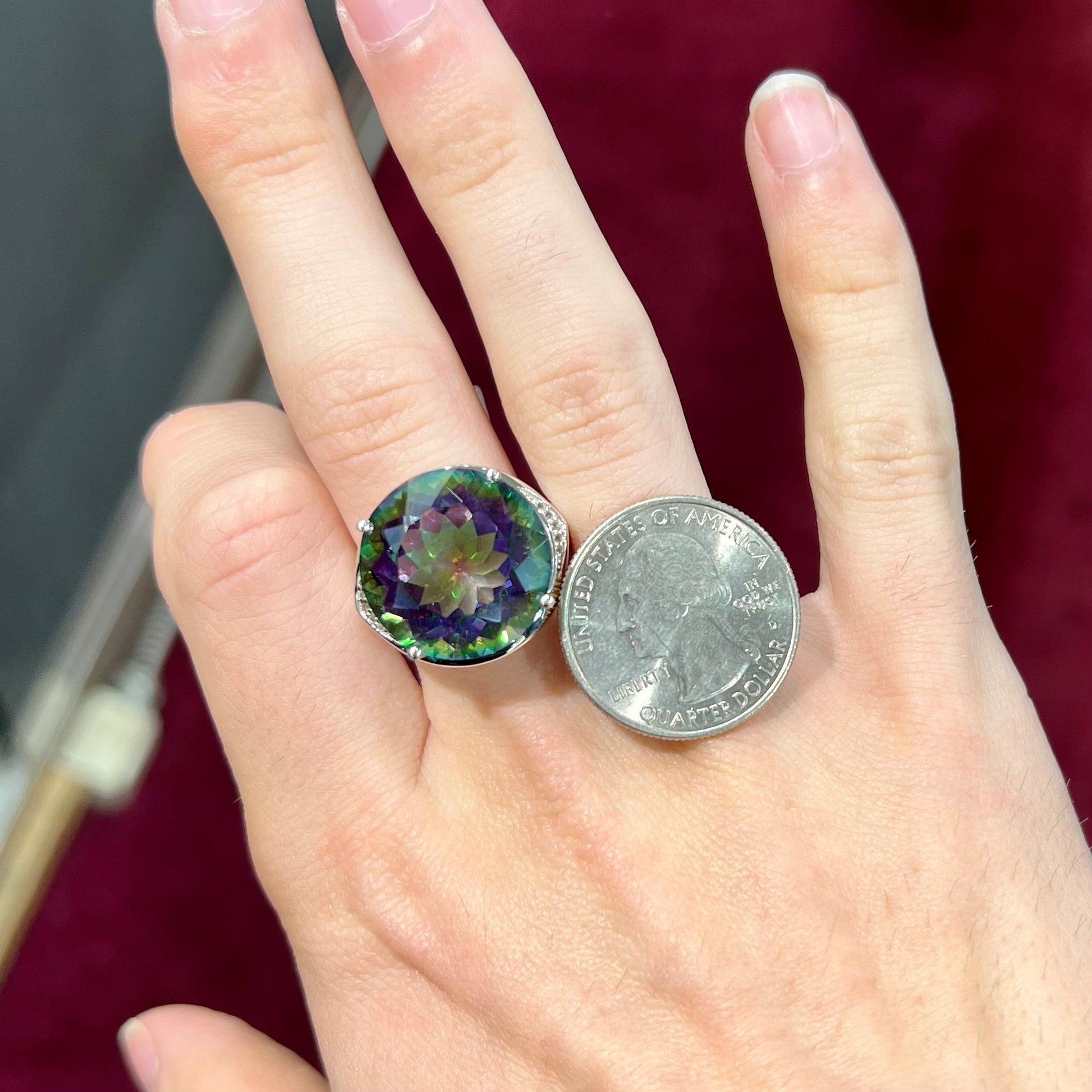A large, round cut pink and green mystic topaz set in a sterling silver ring with white topaz accent stones.