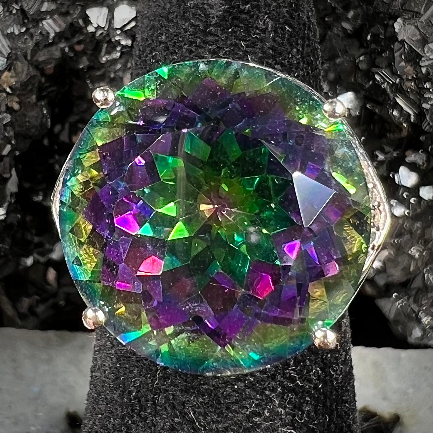A large, round cut pink and green mystic topaz set in a sterling silver ring with white topaz accent stones.