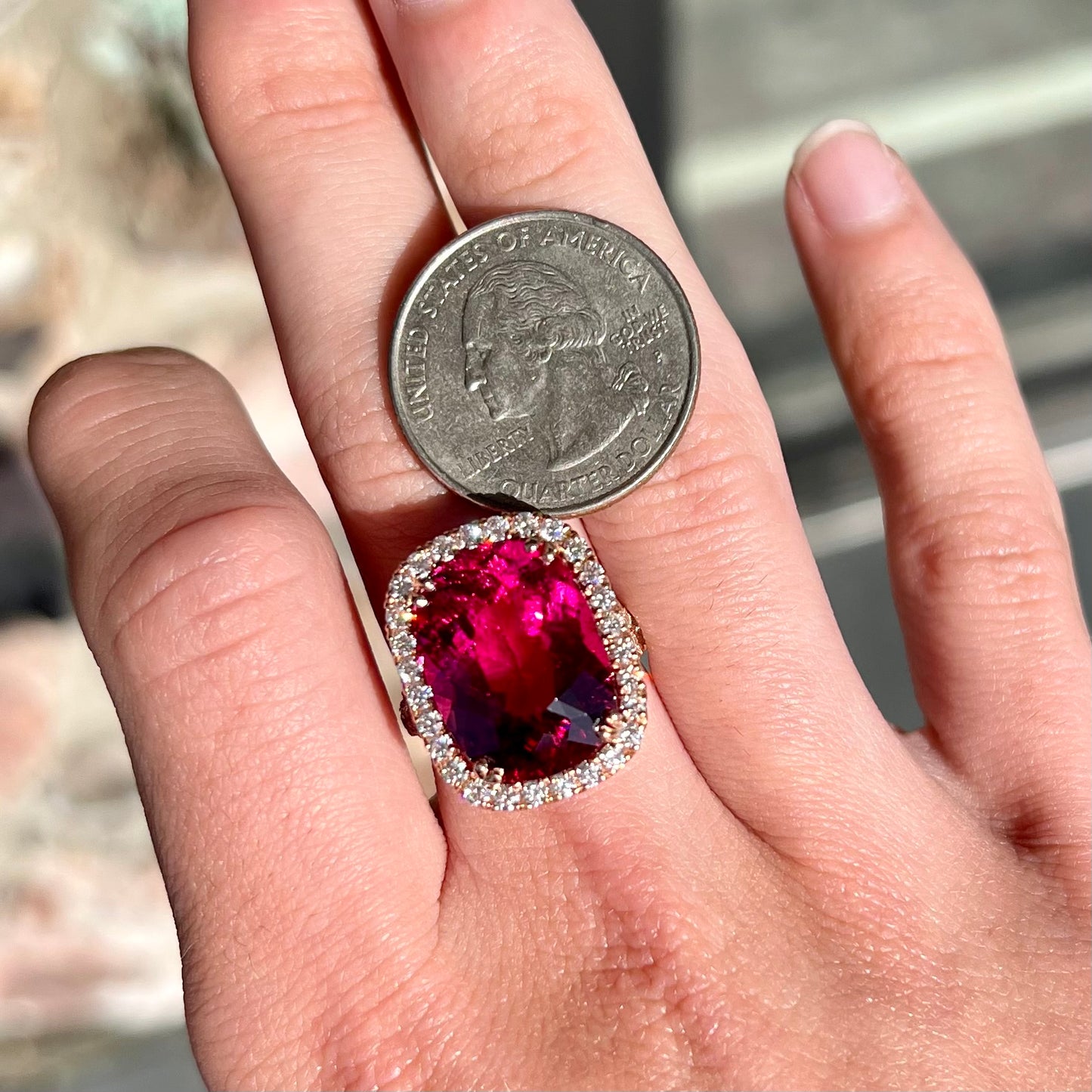 A rose gold, split shank engagement ring set with a cushion cut rubellite tourmaline in a diamond halo.