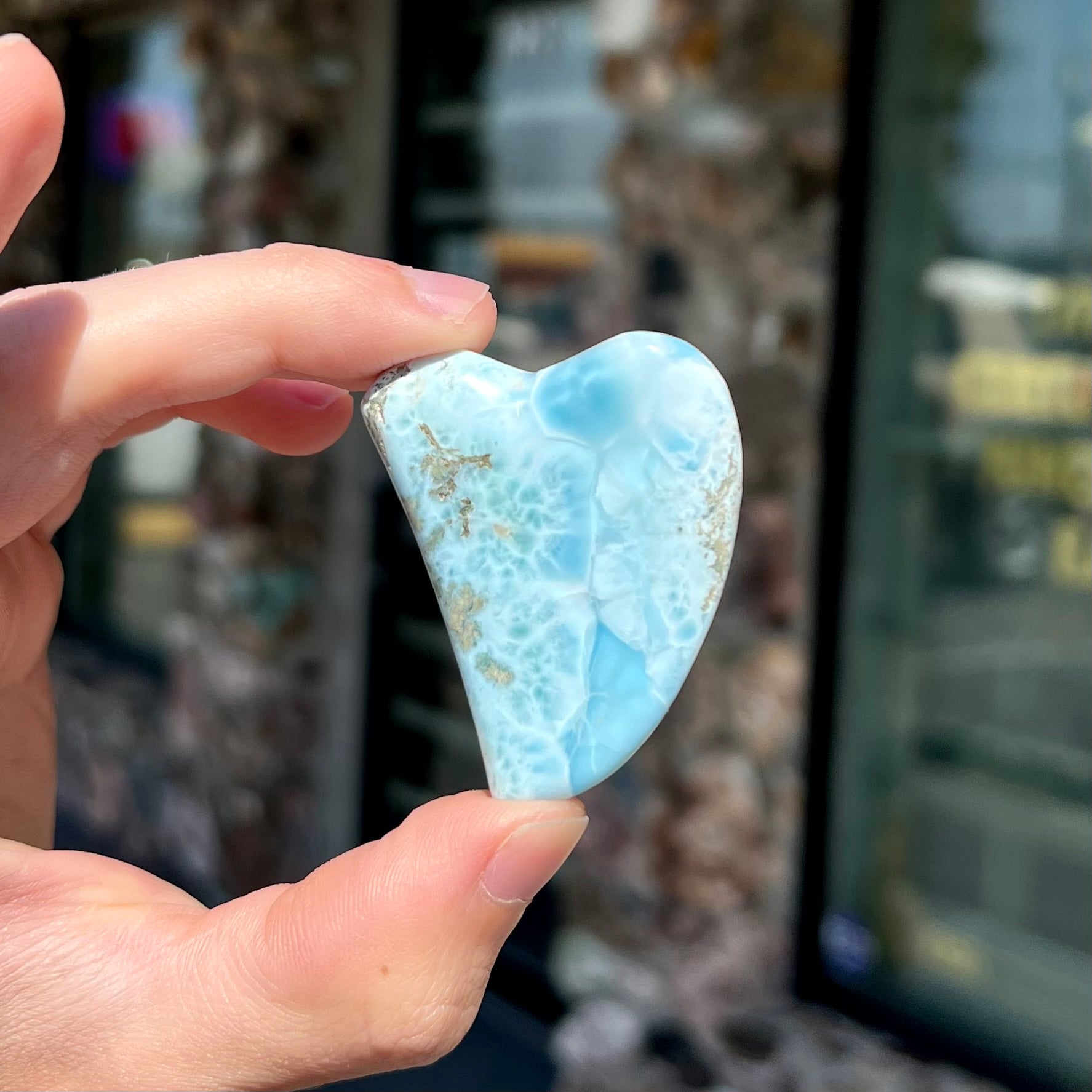 A loose larimar stone that has been hand-carved in the shape of a freeform heart.