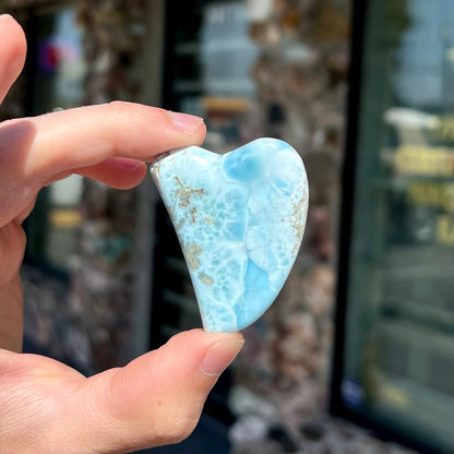 A loose larimar stone that has been hand-carved in the shape of a freeform heart.