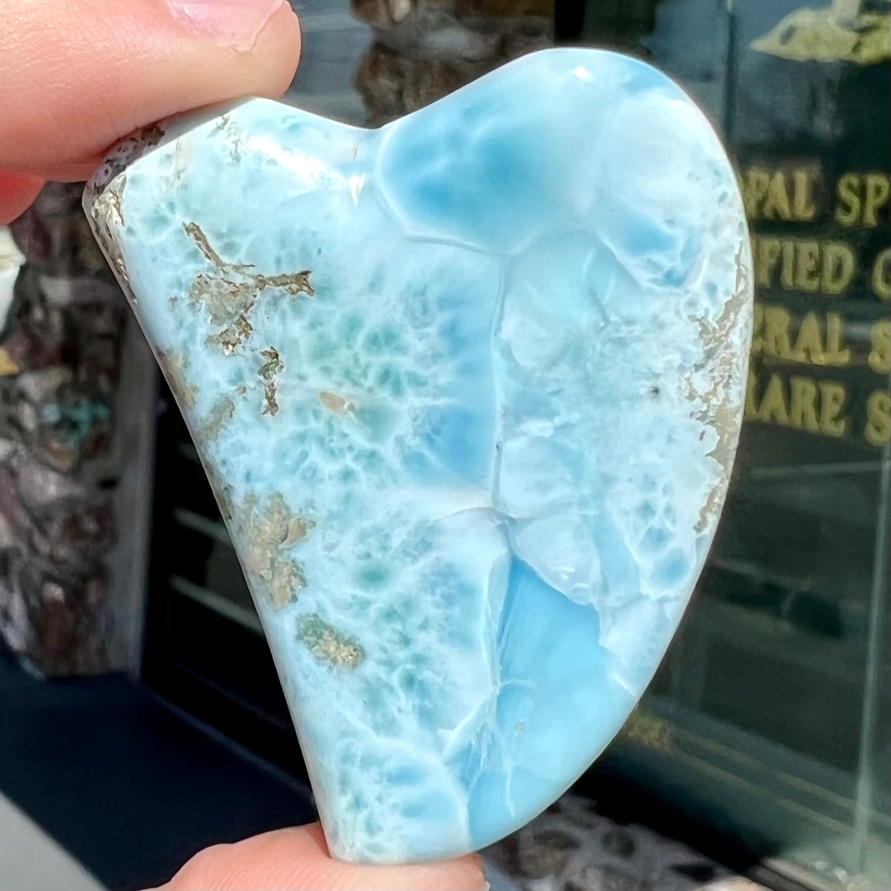 A loose larimar stone that has been hand-carved in the shape of a freeform heart.