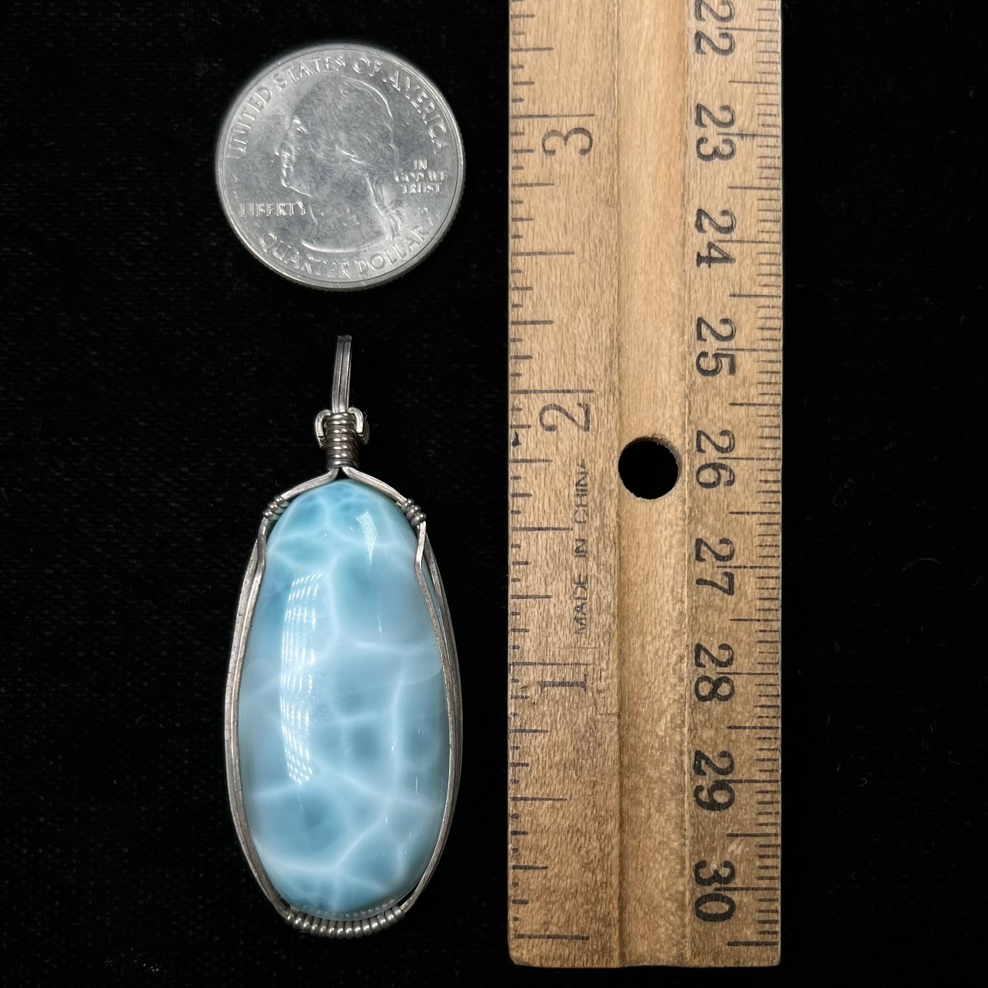A large, oval cabochon cut blue larimar stone mounted in a sterling silver wire wrapped pendant.