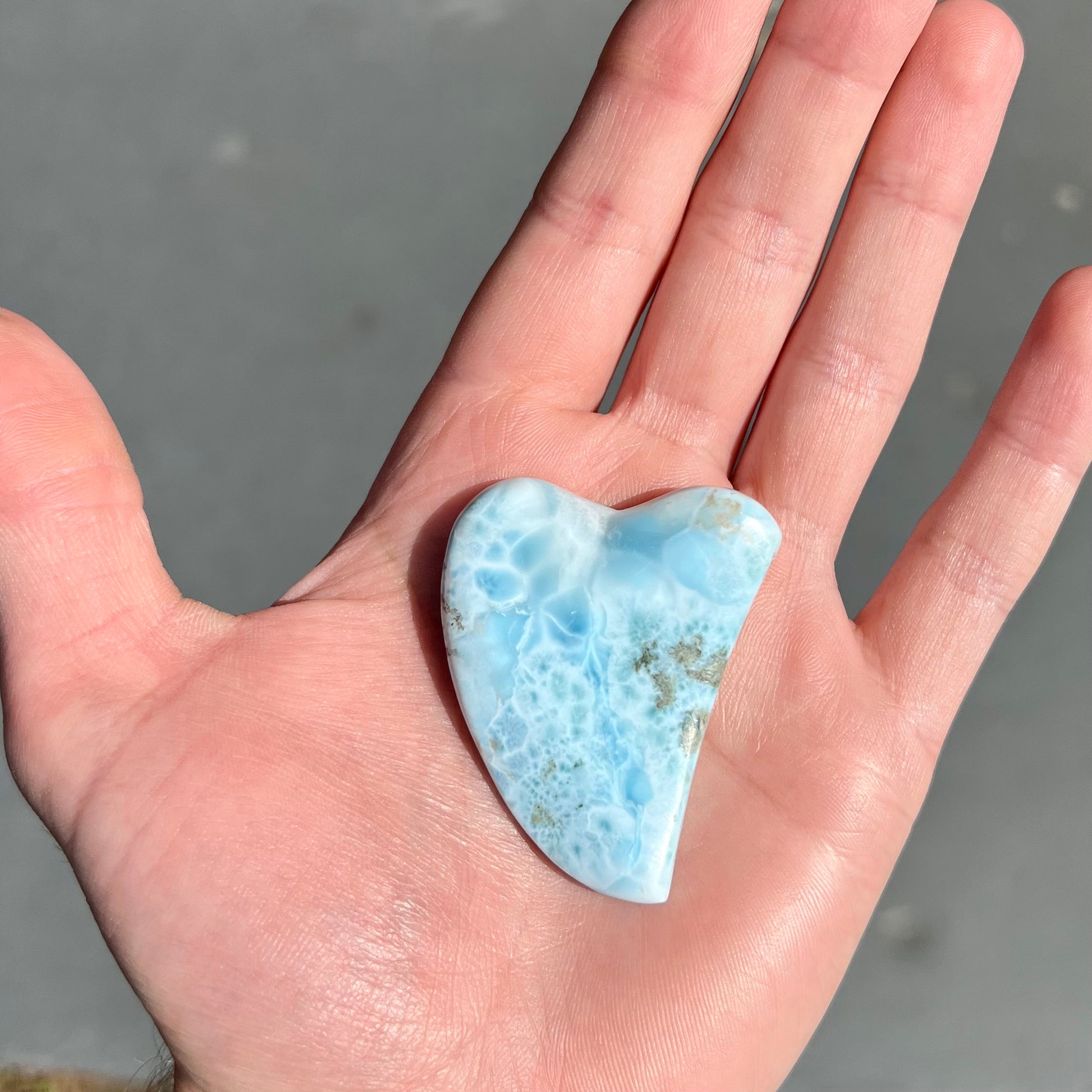 A loose larimar stone that has been hand-carved in the shape of a freeform heart.