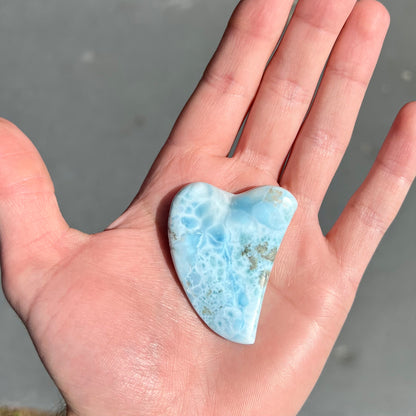 A loose larimar stone that has been hand-carved in the shape of a freeform heart.