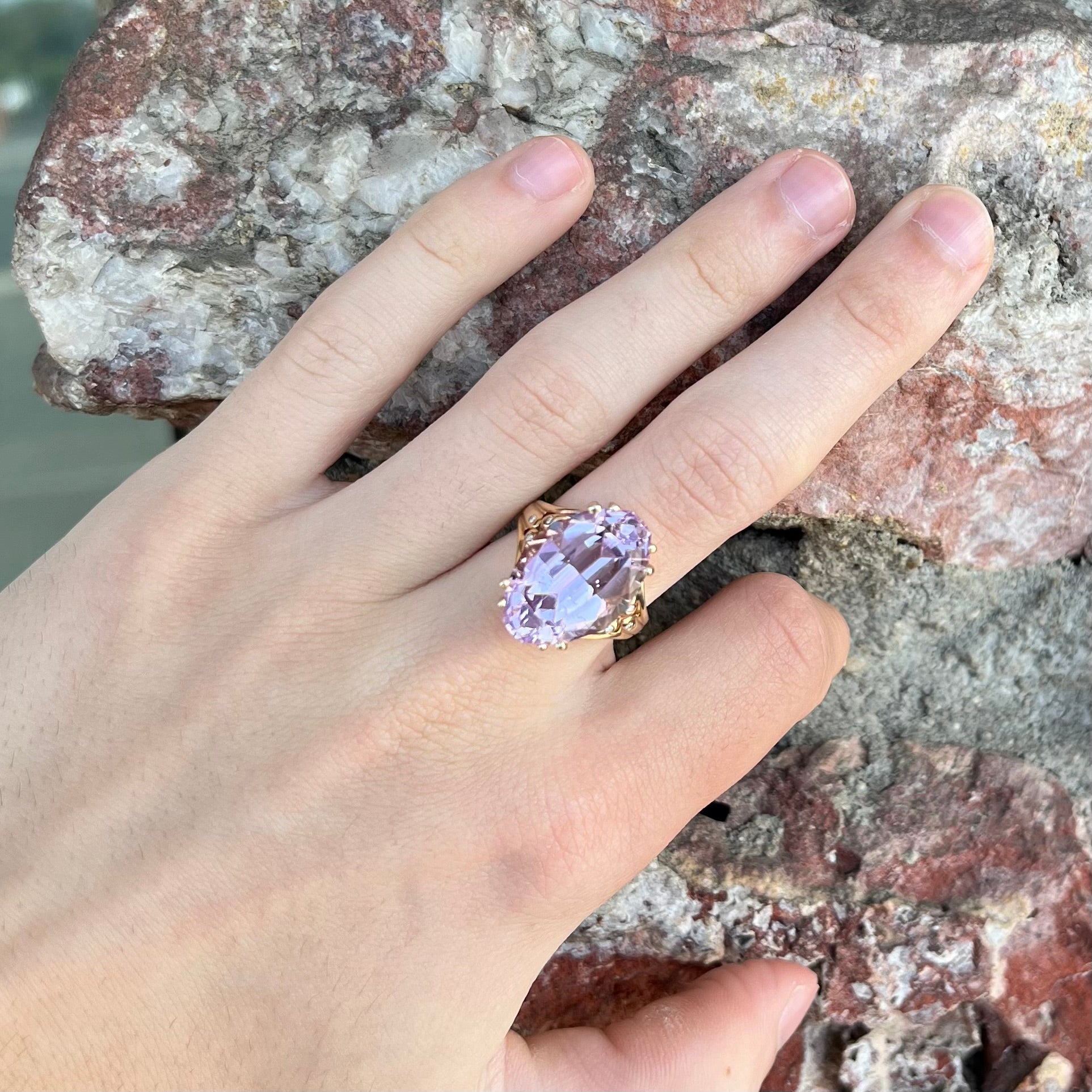 A large, pink kunzite is prong set into a 14kt yellow gold basket-style ring mounting with three diamonds flush set into the design on each side.