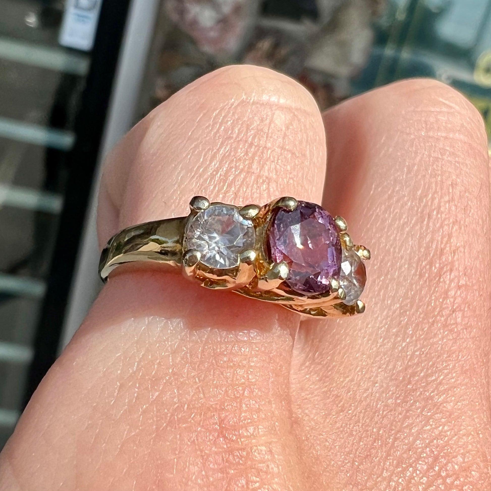 A yellow gold three stone ring set with two round cut white zircons and one cushion cut purple spinel.