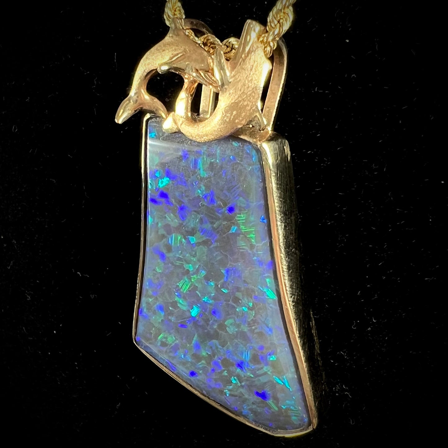 A gold freeform cut black opal bezel pendant cast with two dolphins on top of the opal.