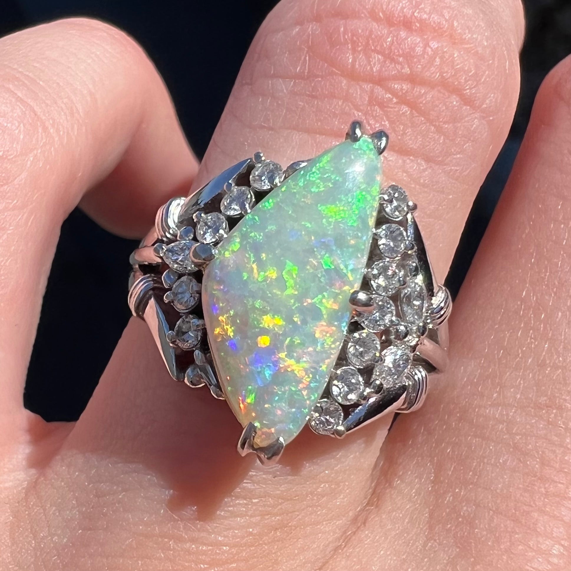 A freeform triangular cabochon cut Lightning Ridge white crystal opal set with diamonds in an ornate platinum split shank setting.