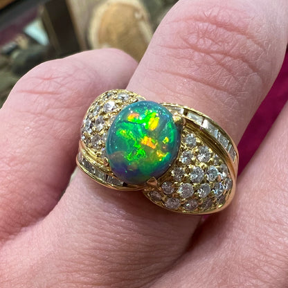 An 18kt yellow gold oval cabochon cut Lightning Ridge black opal ring.  The shank is set with round and baguette cut diamonds.
