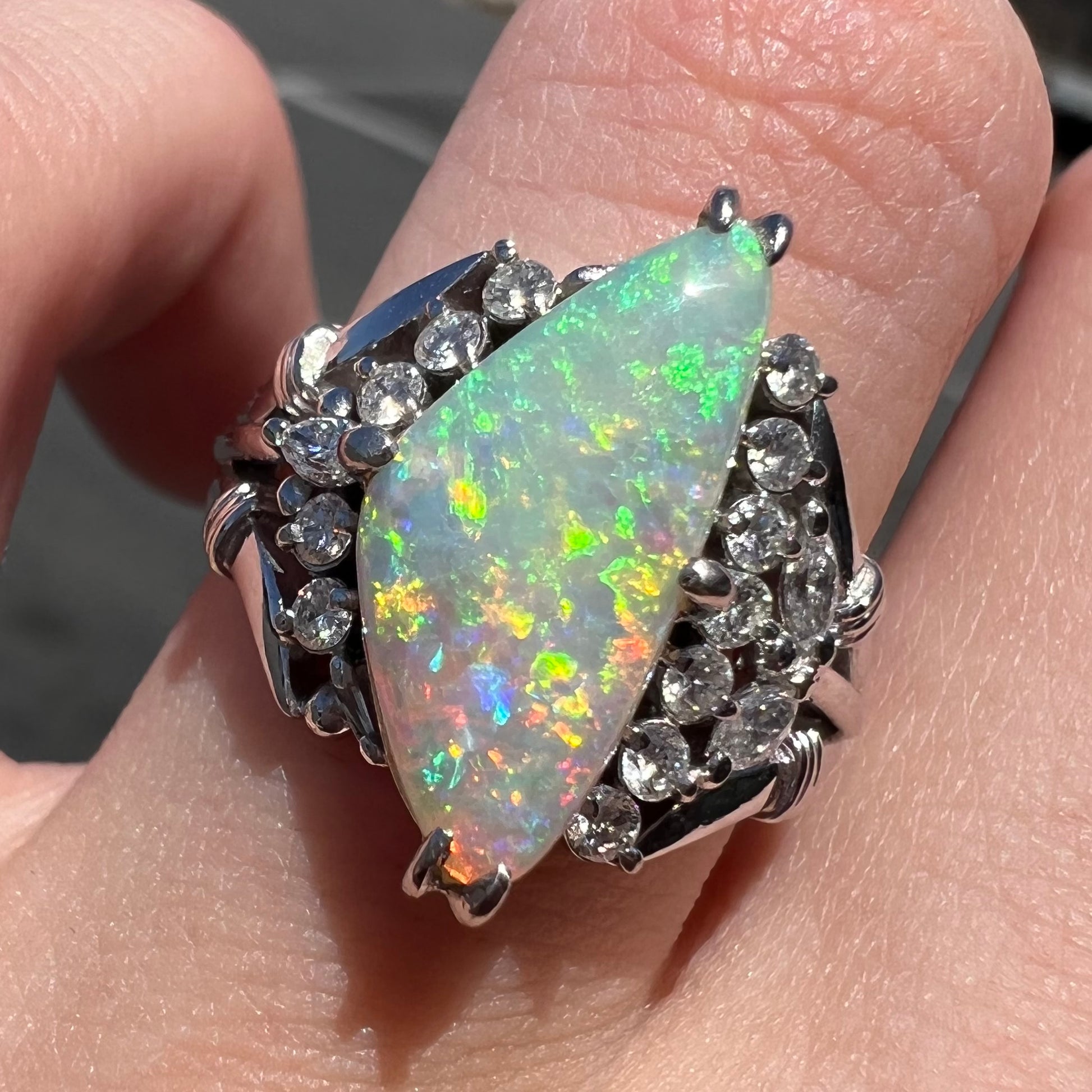 A freeform triangular cabochon cut Lightning Ridge white crystal opal set with diamonds in an ornate platinum split shank setting.
