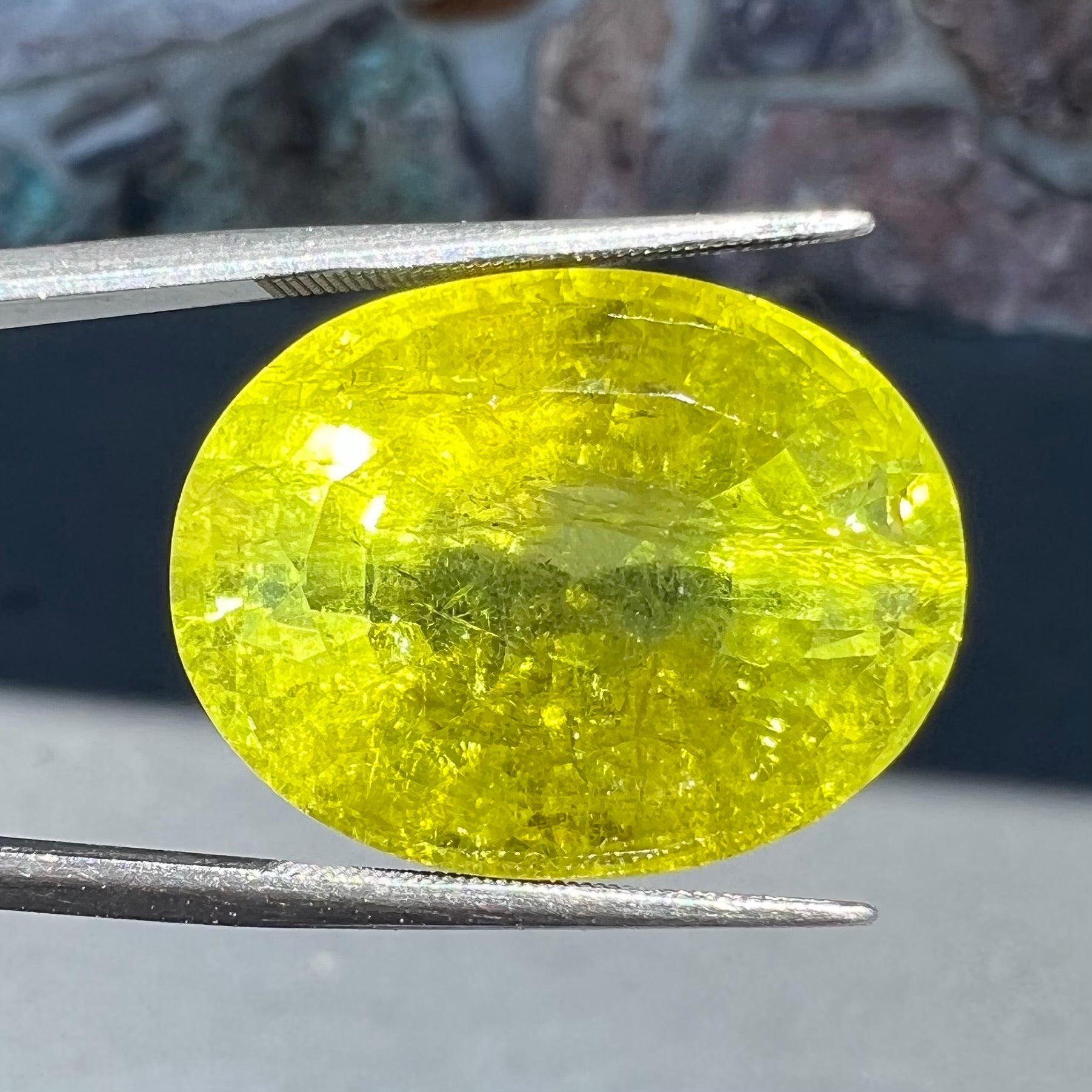 A loose, faceted oval cut green tourmaline stone.  The color is an almost neon yellow-green.
