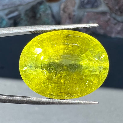 A loose, faceted oval cut green tourmaline stone.  The color is an almost neon yellow-green.