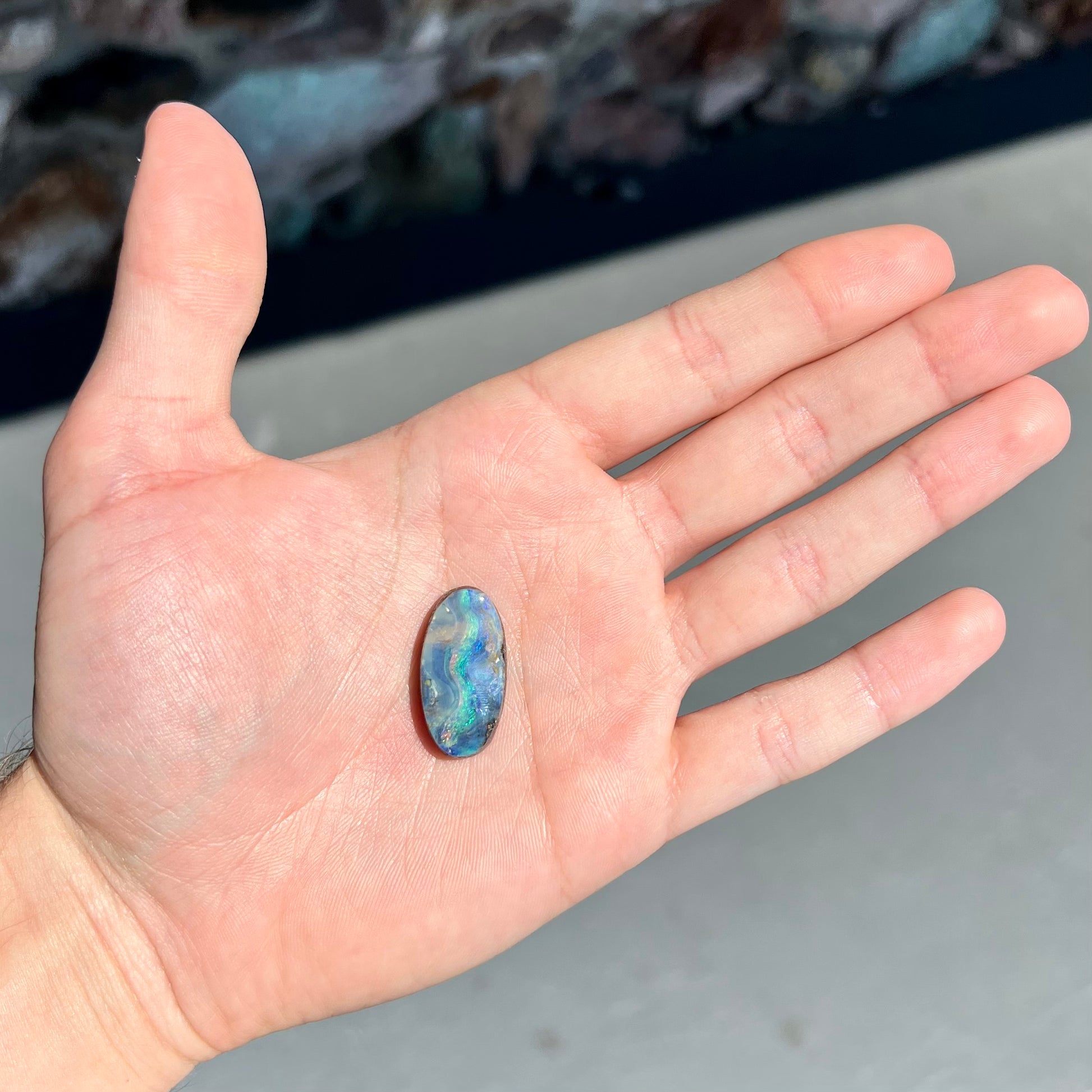 A loose, oval cabochon cut Quilpie boulder opal from Queensland, Australia.  The stone is blue with green fire.