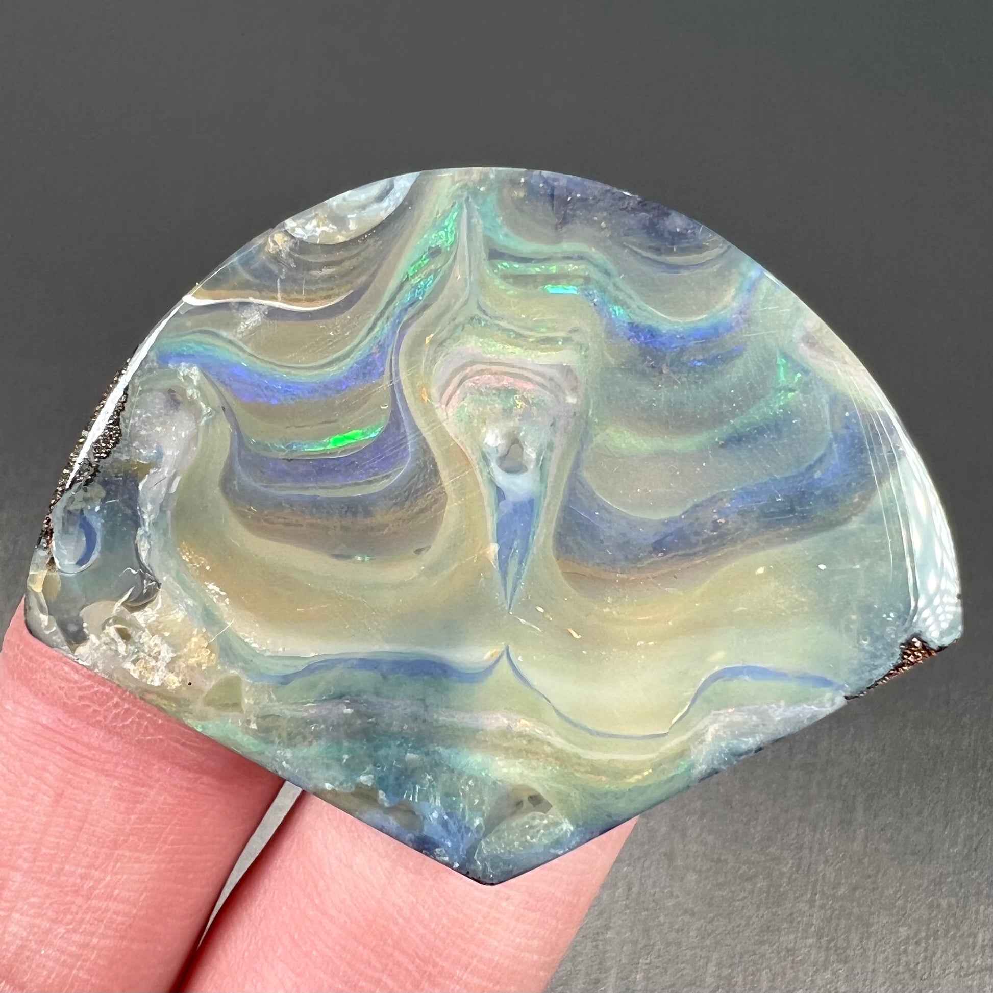 A polished, loose boulder opal stone from Queensland, Australia.  Fire colors are green, blue, purple, and salmon.