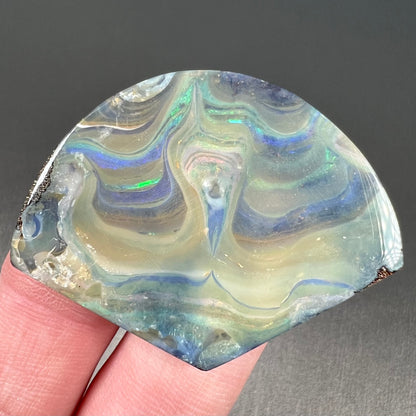 A polished, loose boulder opal stone from Queensland, Australia.  Fire colors are green, blue, purple, and salmon.