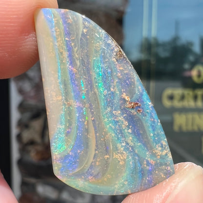 A polished, freeform shaped boulder opal stone from Queensland, Australia.  Predominant colors are green, blue, and violet.