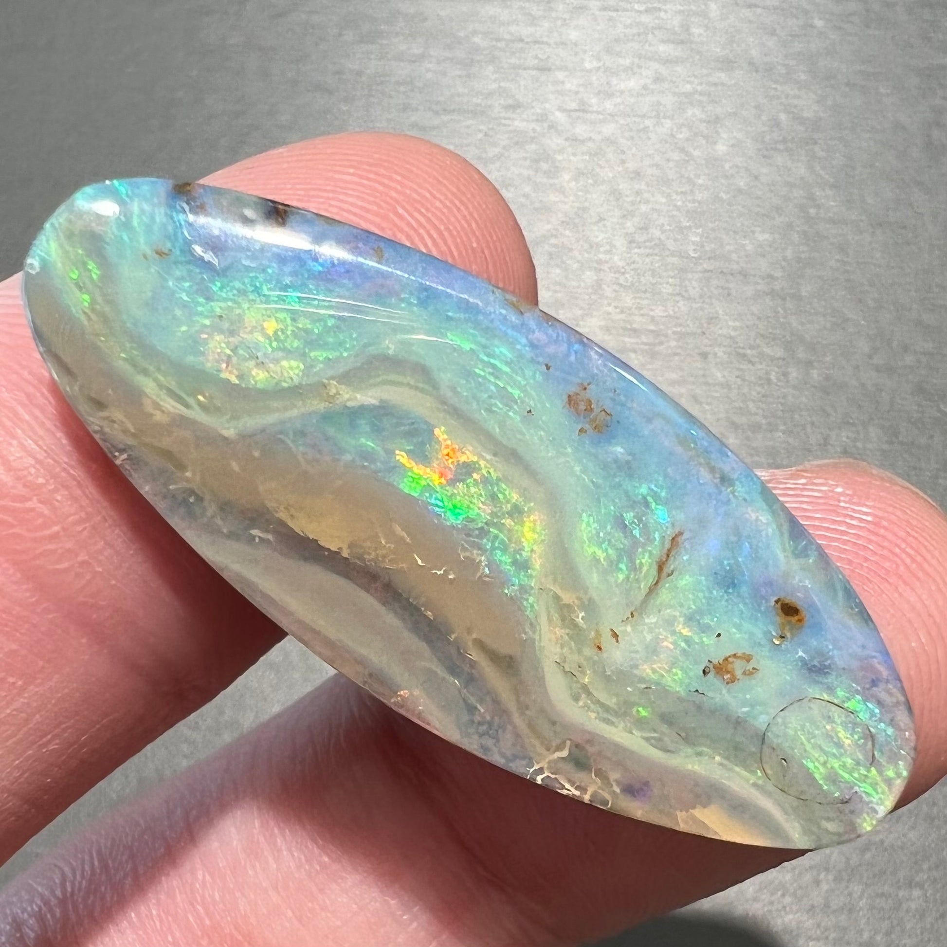 A loose, oval cabochon cut opal from Quilpie, Australia.  Blue, red, and green colors can be seen.