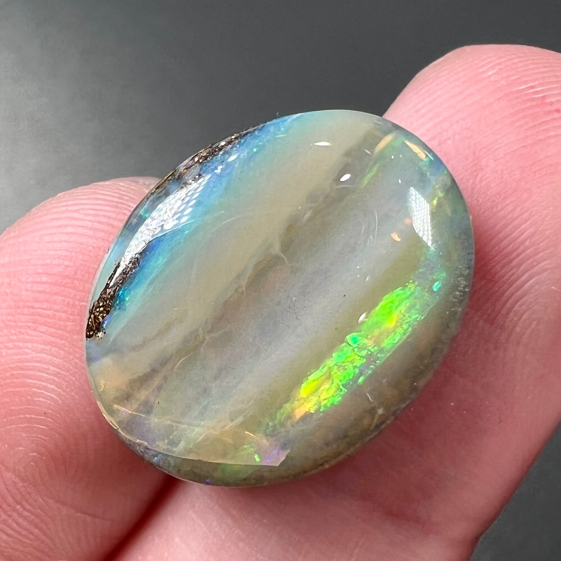 A loose, oval cabochon cut Quilpie boulder opal stone from Queensland, Australia.  The predominant color flash is green.
