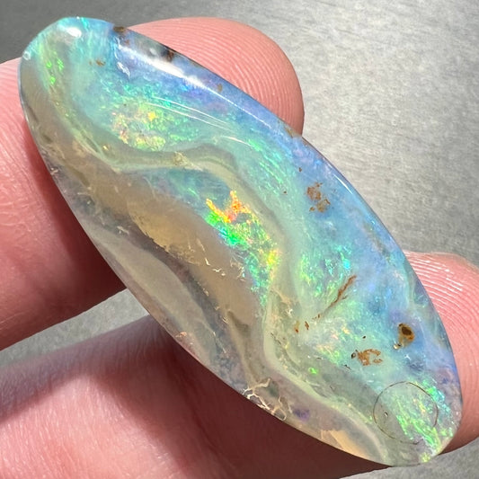 A loose, oval cabochon cut opal from Quilpie, Australia.  Blue, red, and green colors can be seen.