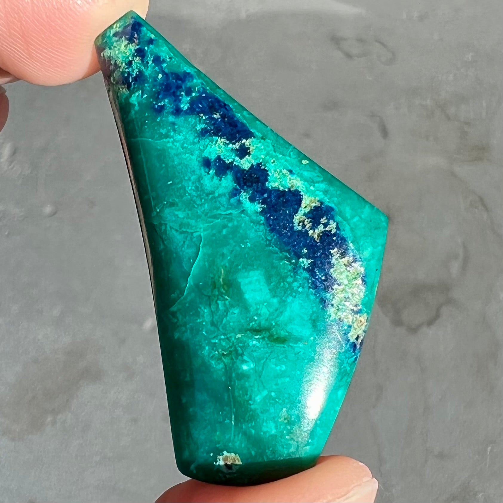 A loose triangular freeform cabochon cut green chrysocolla with blue azurite inclusions.