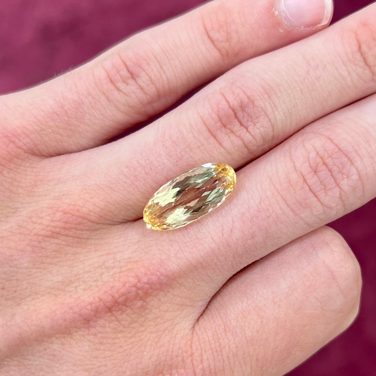 A loose, oval cut golden topaz gemstone.  A stronger concentration of yellow rests in the edges of the stone.