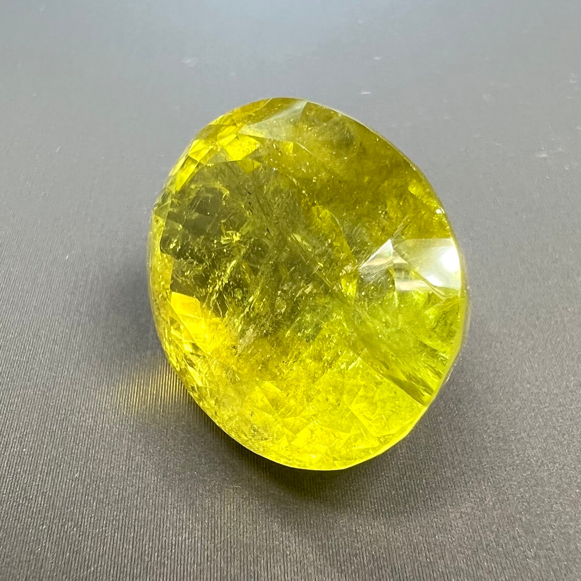 A loose, faceted oval cut green tourmaline stone.  The color is an almost neon yellow-green.