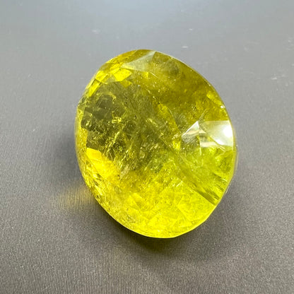 A loose, faceted oval cut green tourmaline stone.  The color is an almost neon yellow-green.