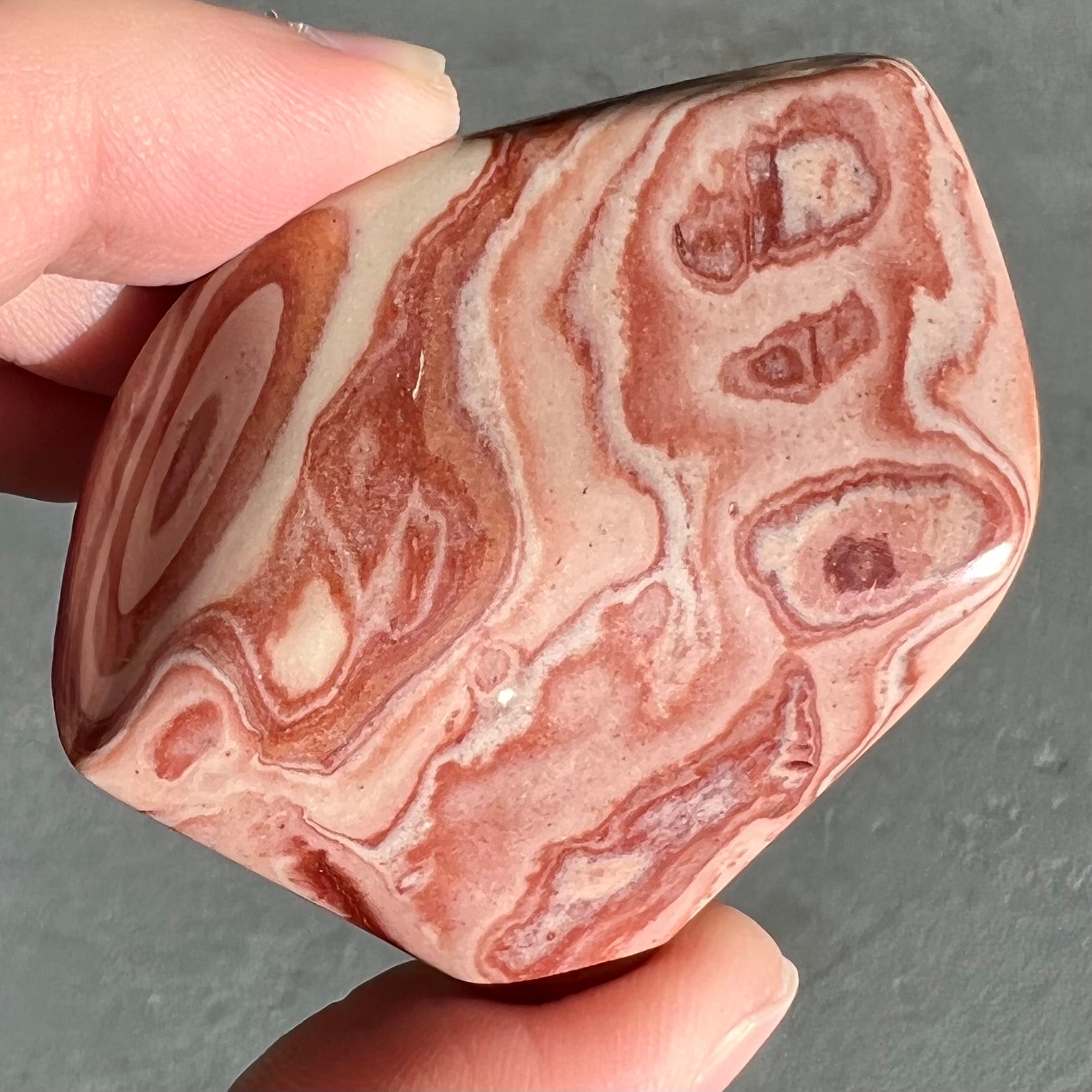 A polished piece of pinkish red picture jasper.  The stone displays a bull's eye pattern.