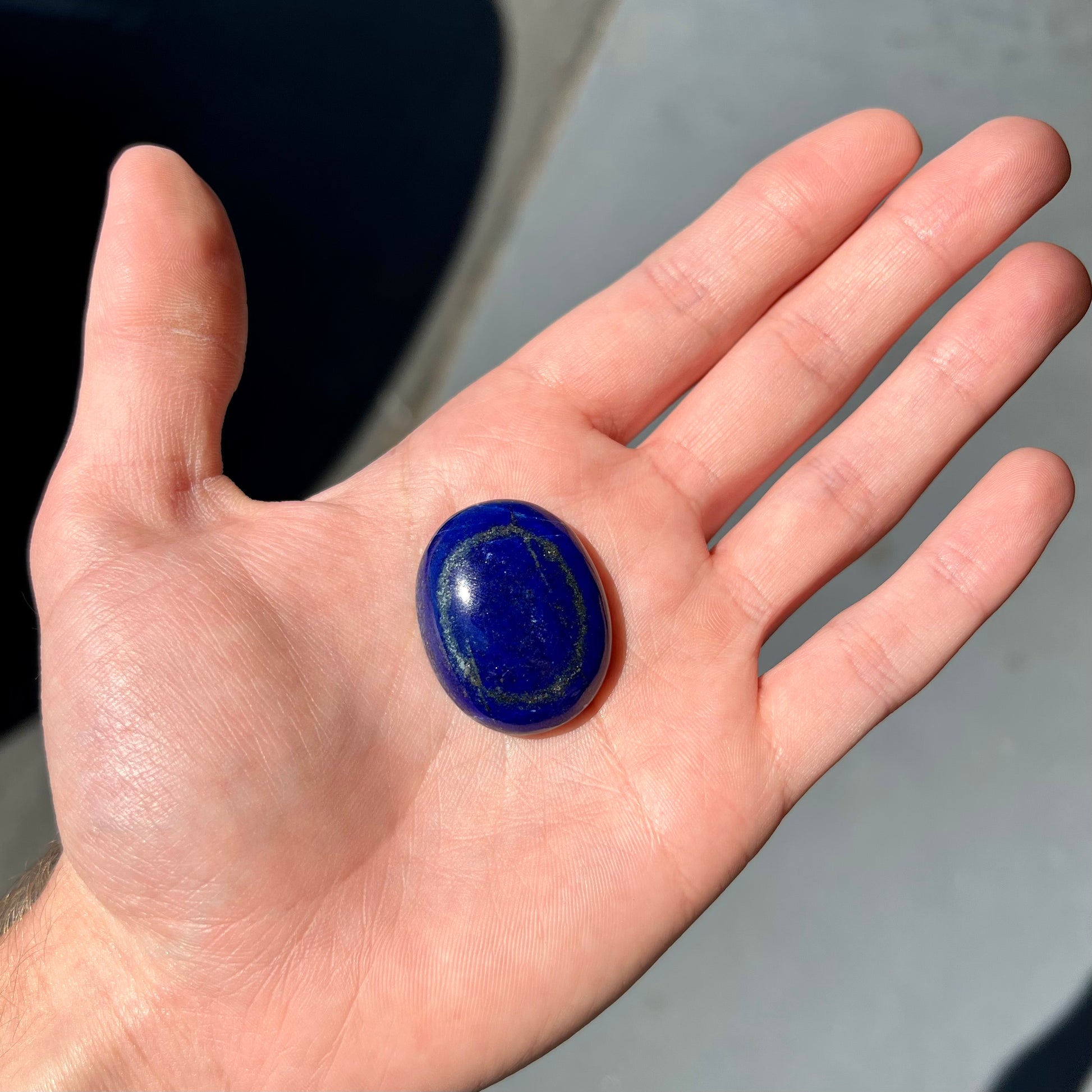 A loose, oval cabochon cut lapis lazuli stone.  A circle of pyrite inclusions is seen on the front.