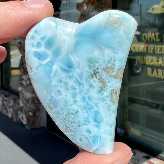 A loose larimar stone that has been hand-carved in the shape of a freeform heart.