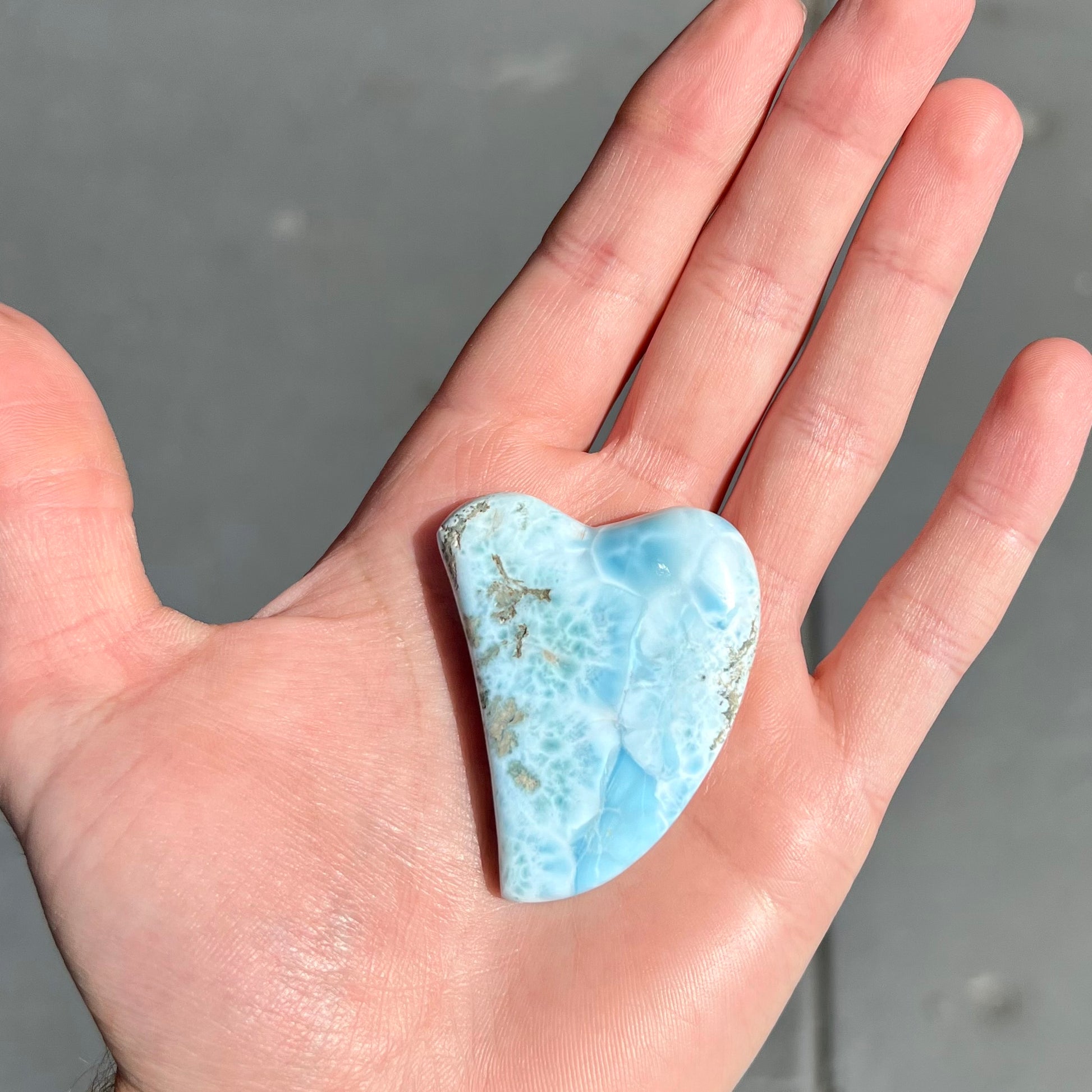 A loose larimar stone that has been hand-carved in the shape of a freeform heart.