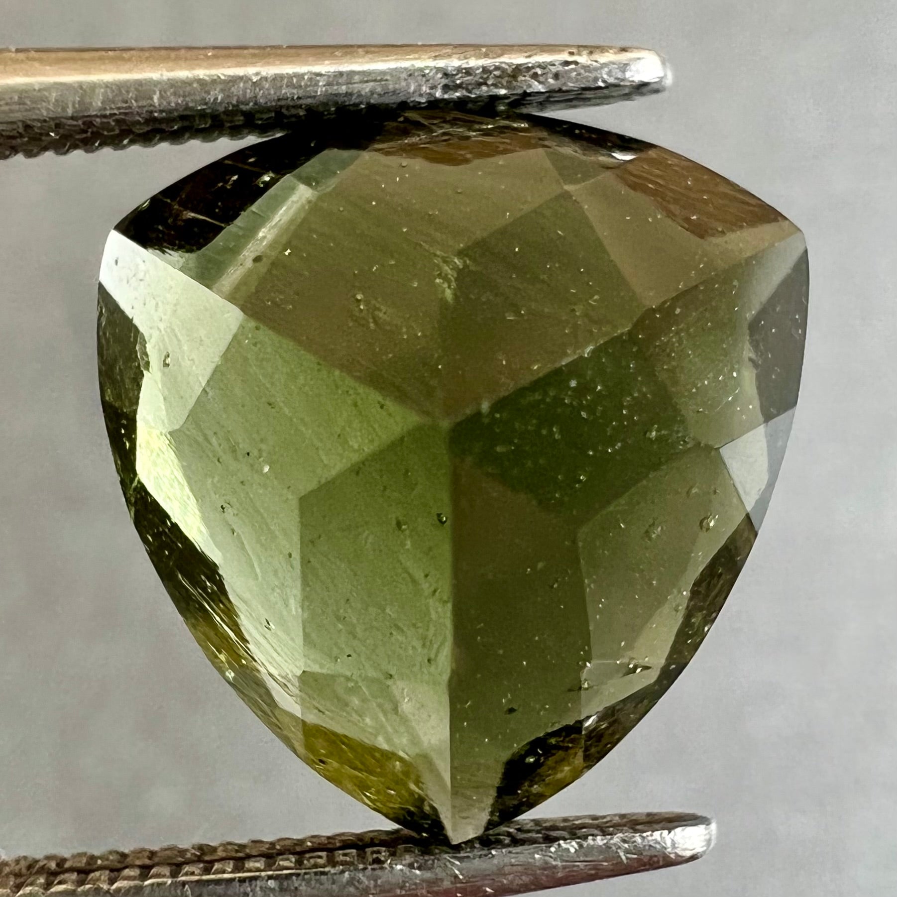 A loose, faceted trillion cut moldavite stone that weighs 2.73 carats.