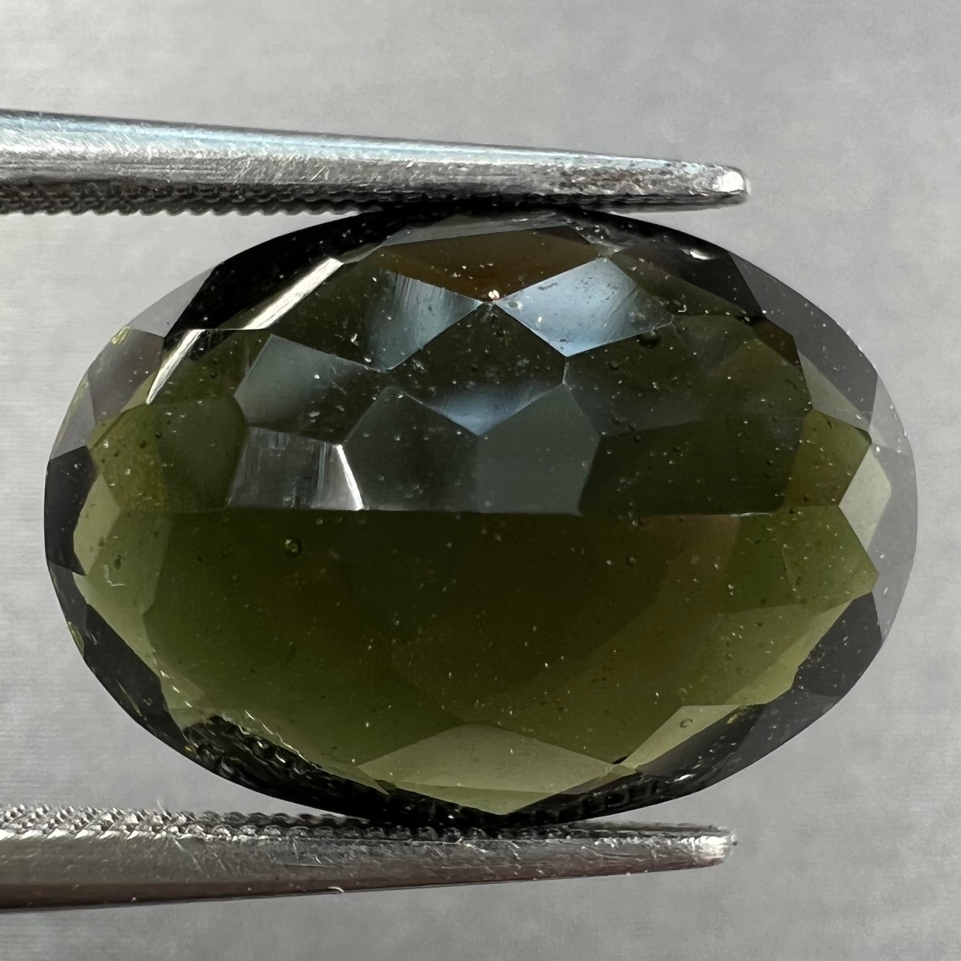 A loose faceted oval checkerboard cut moldavite stone.