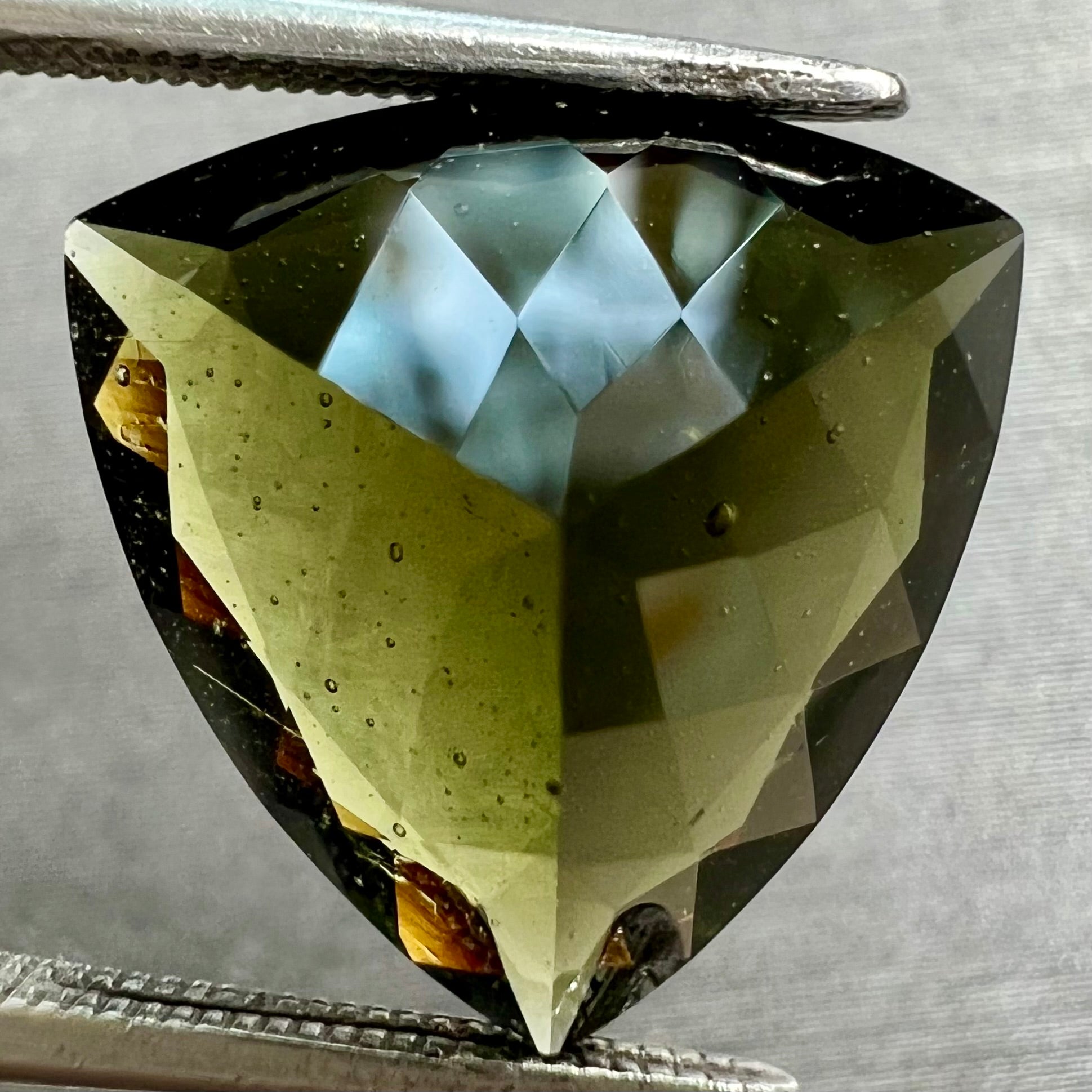 A faceted trillion cut moldavite gemstone that weighs 3.98 carats.  The stone is a dark green color.