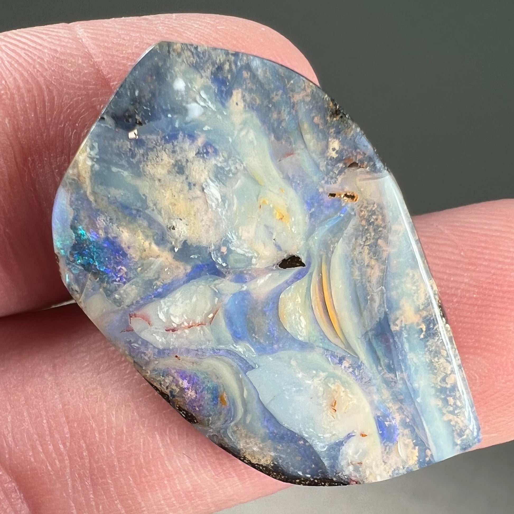 A loose, polished, freeform cut boulder opal stone from Queensland, Australia.