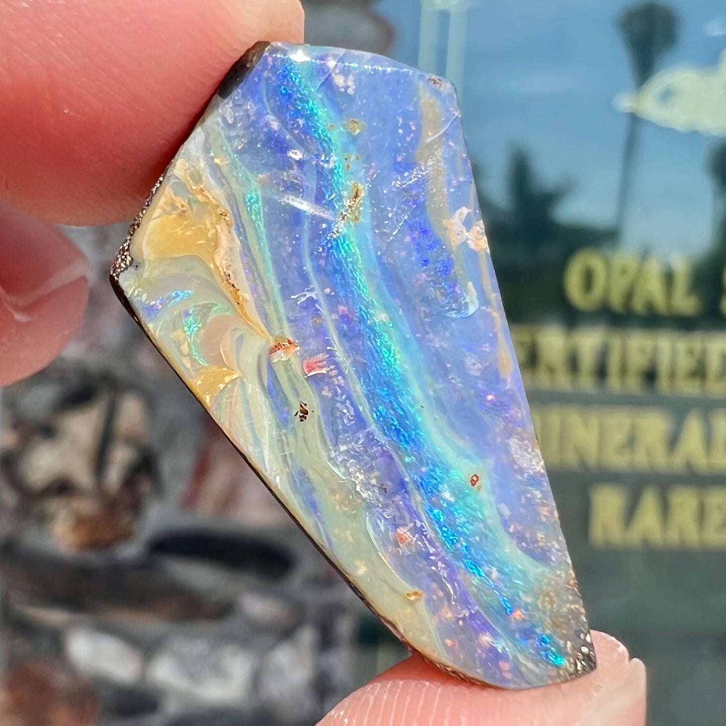 A loose, polished, freeform cut boulder opal stone from Queensland, Australia.