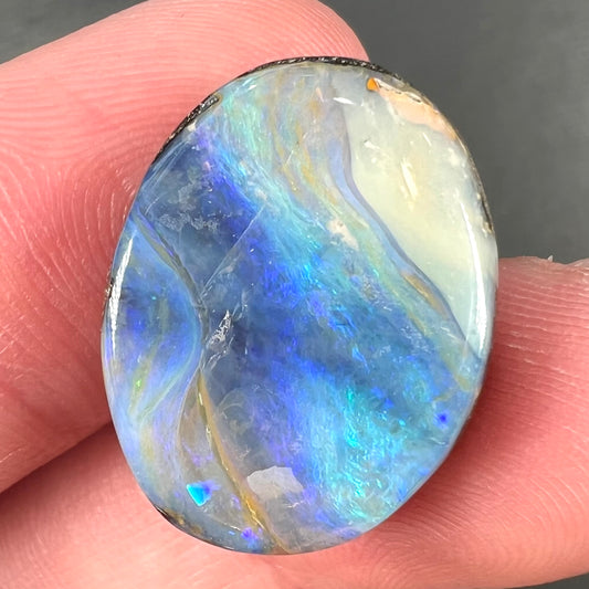 A loose, oval cabochon cut Australian boulder opal stone.