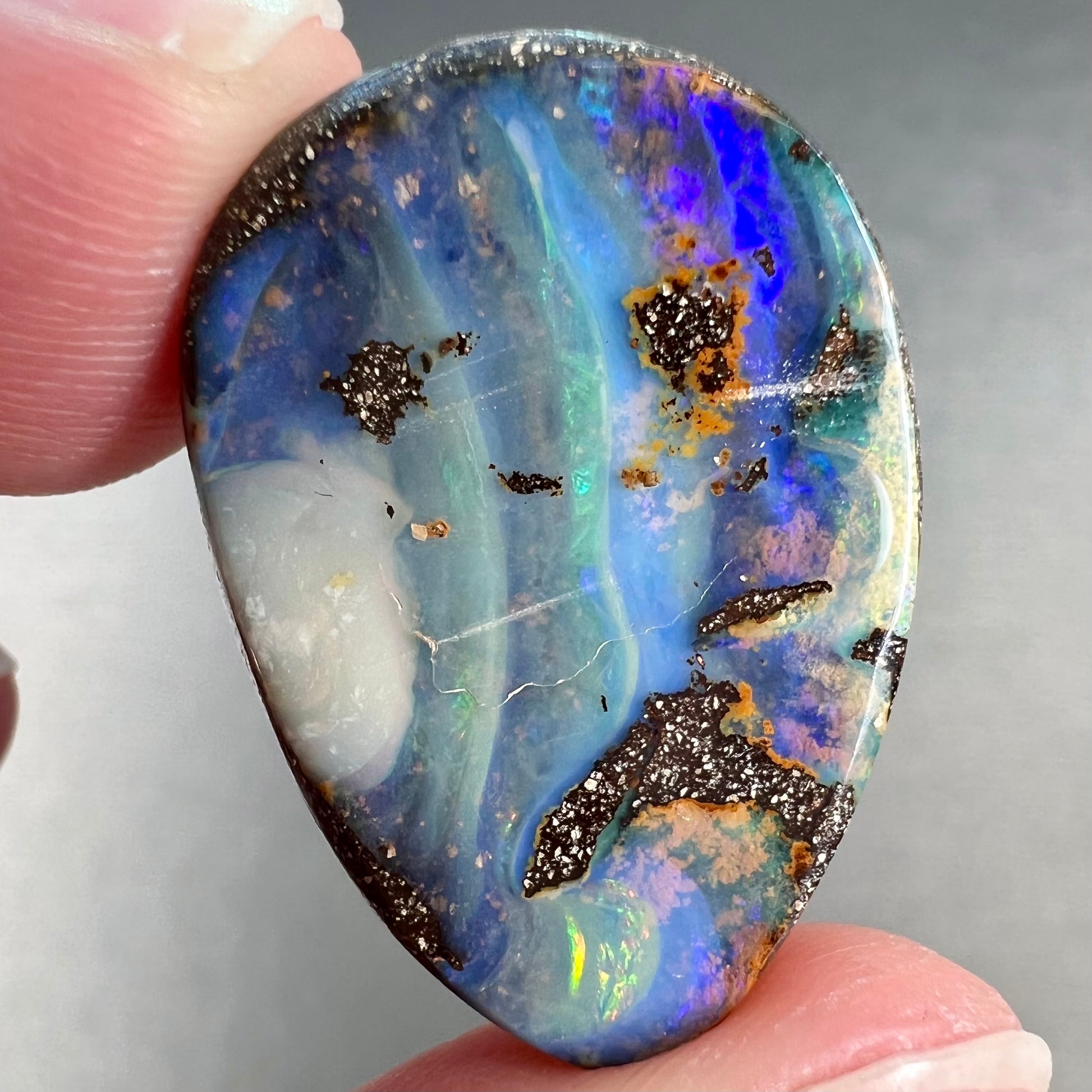 A loose, pear shaped Australian boulder opal.  The pattern on the opal resembles the face of a very sad man.