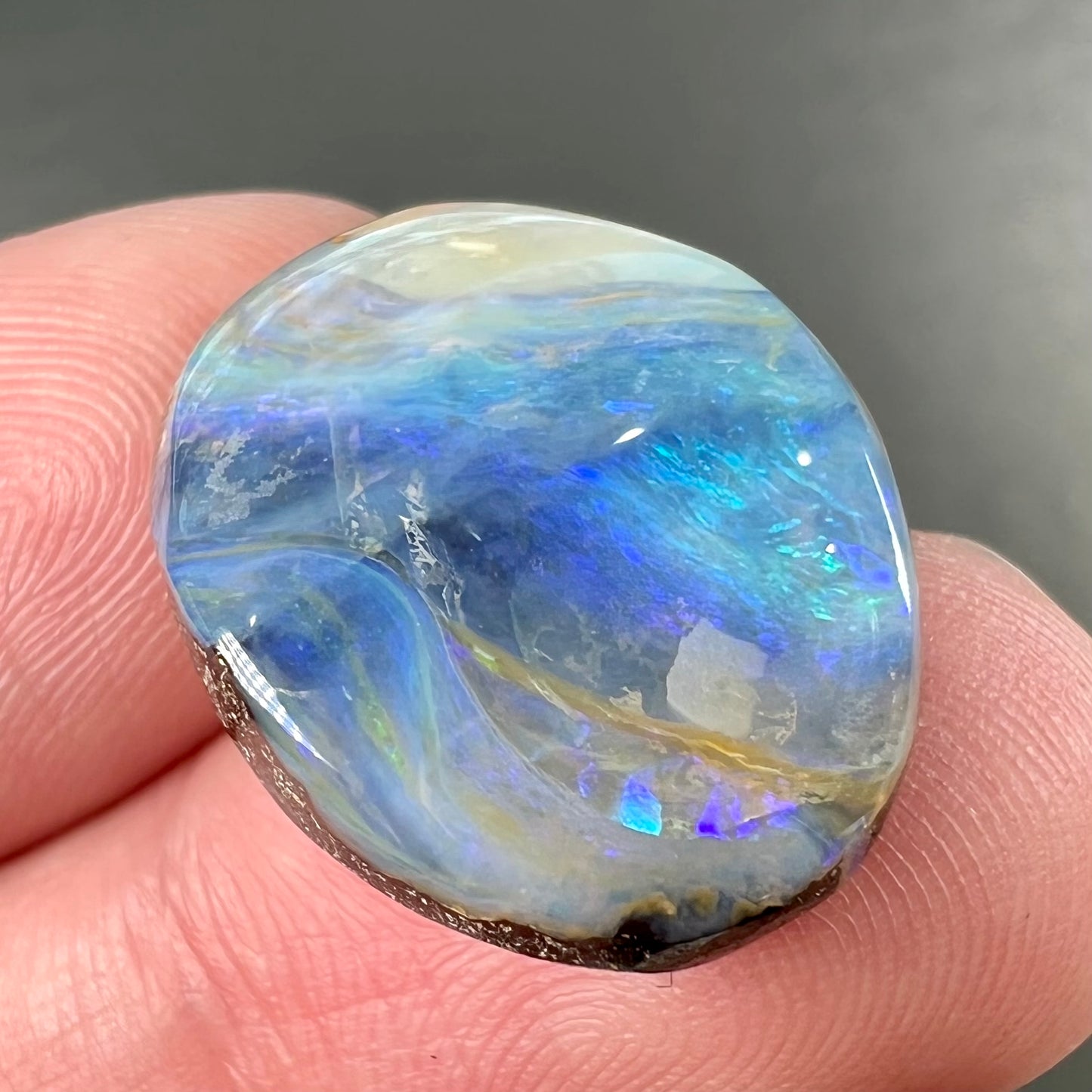 A loose, oval cabochon cut Australian boulder opal stone.