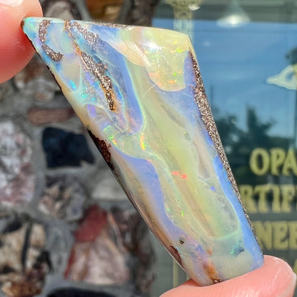 A freeform shaped, polished boulder opal stone from Queensland, Australia.  The stone has red, orange, green, and blue fire.