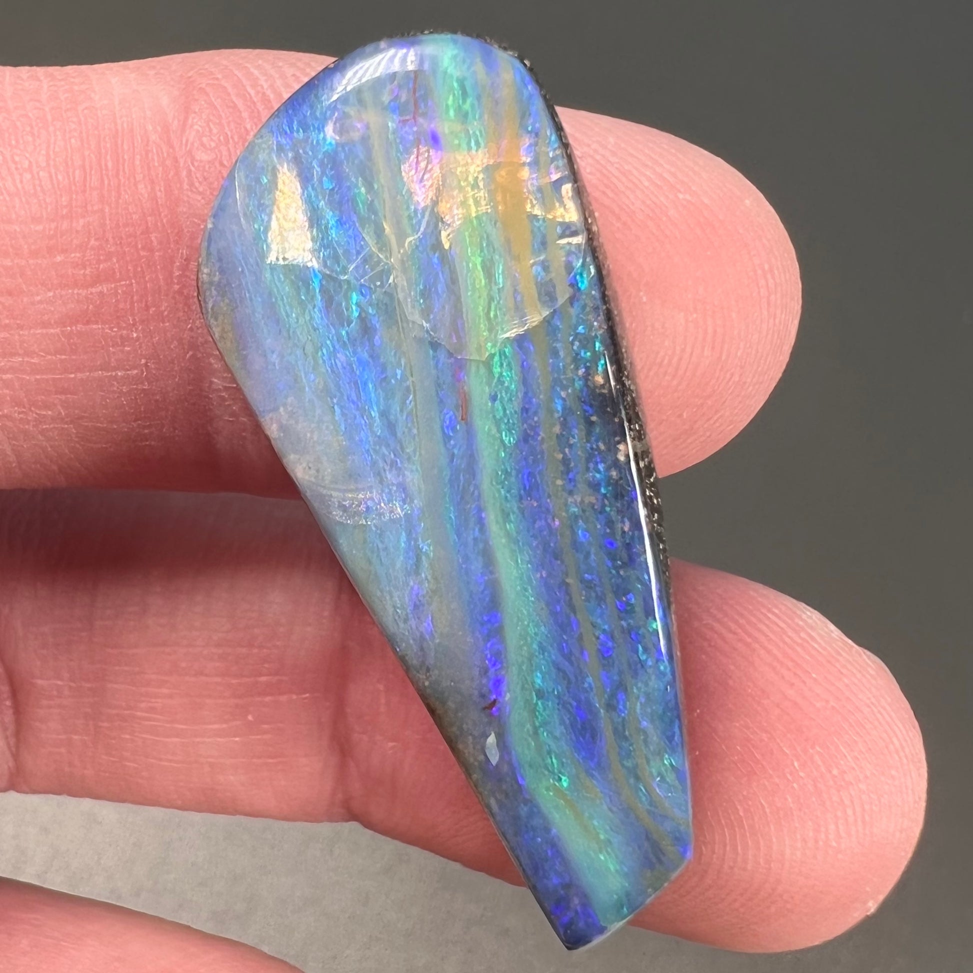 A loose, polished, freeform drop shaped boulder opal stone from Quilpie, Australia.