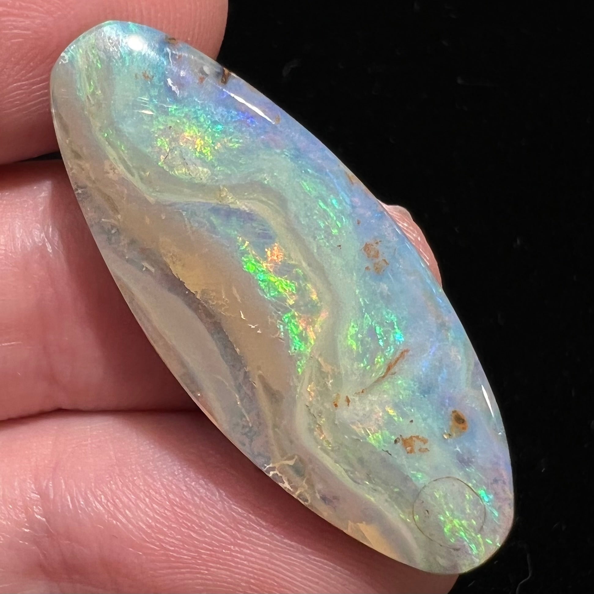 A loose, oval cabochon cut opal from Quilpie, Australia.  Blue, red, and green colors can be seen.