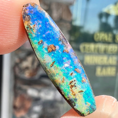 A loose, oval cabochon cut Australian boulder opal from Quilpie, Australia.  Predominant colors are blue and green.