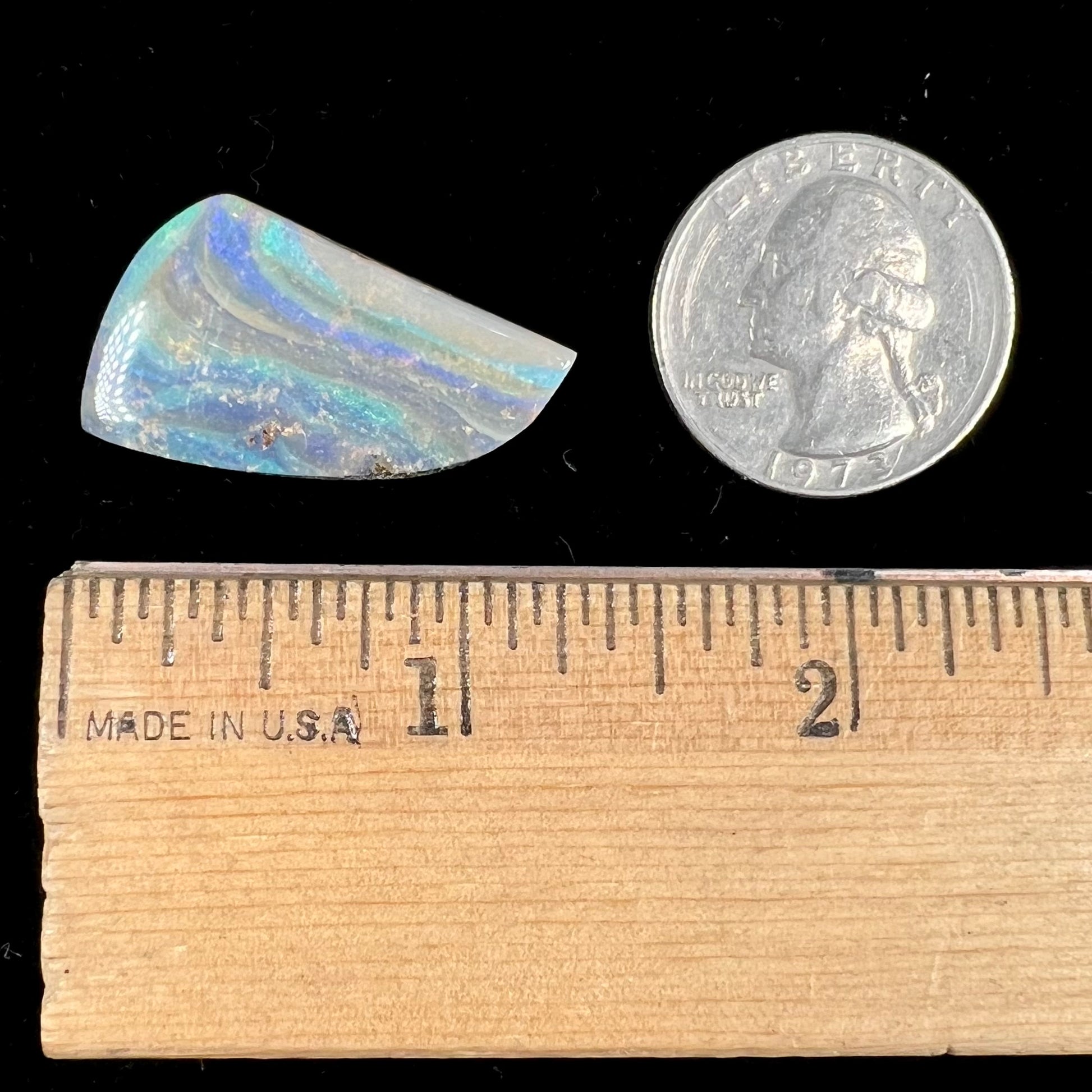 A polished, freeform shaped boulder opal stone from Queensland, Australia.  Predominant colors are green, blue, and violet.