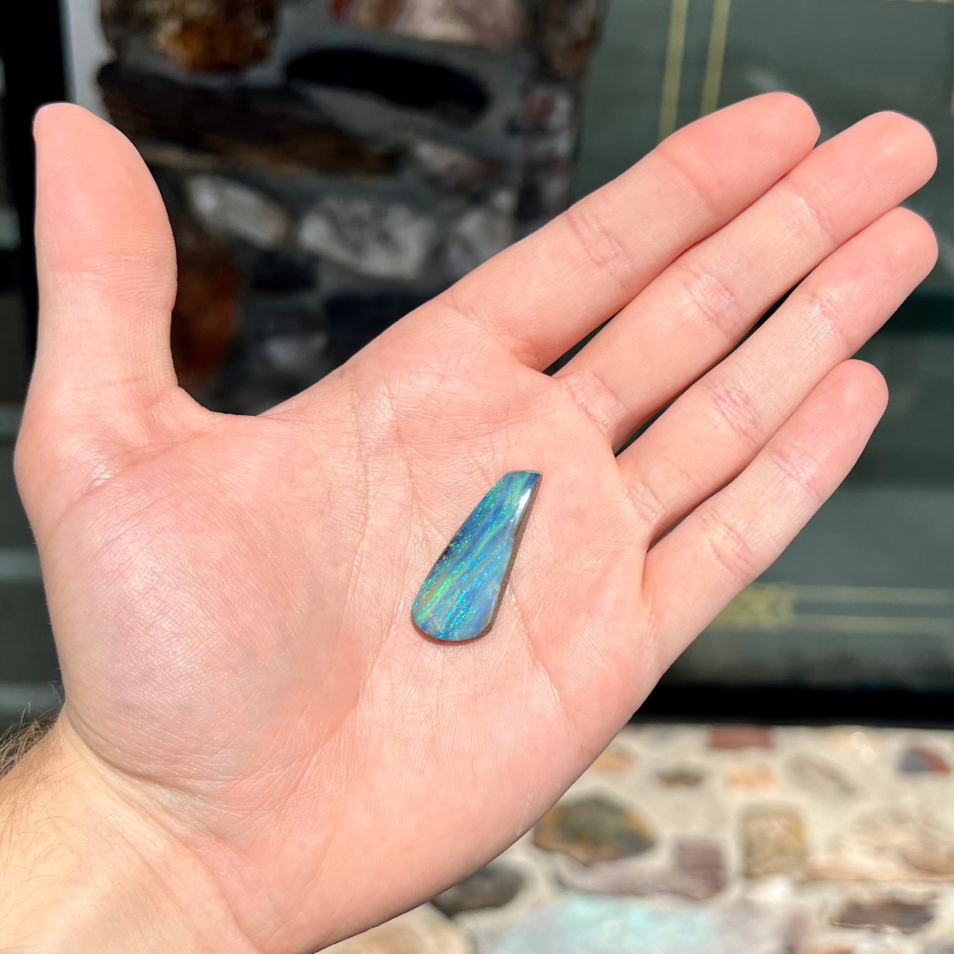 A loose, polished, freeform drop shaped boulder opal stone from Quilpie, Australia.