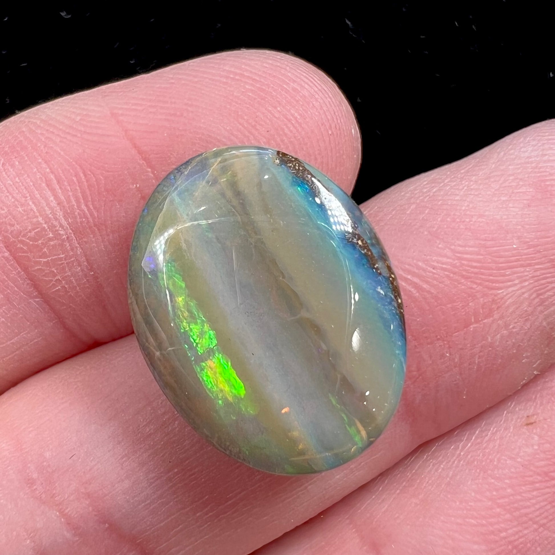 A loose, oval cabochon cut Quilpie boulder opal stone from Queensland, Australia.  The predominant color flash is green.
