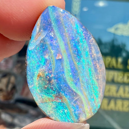 A loose, pear shaped Australian boulder opal stone.  The predominant colors are purple, green, and aqua.