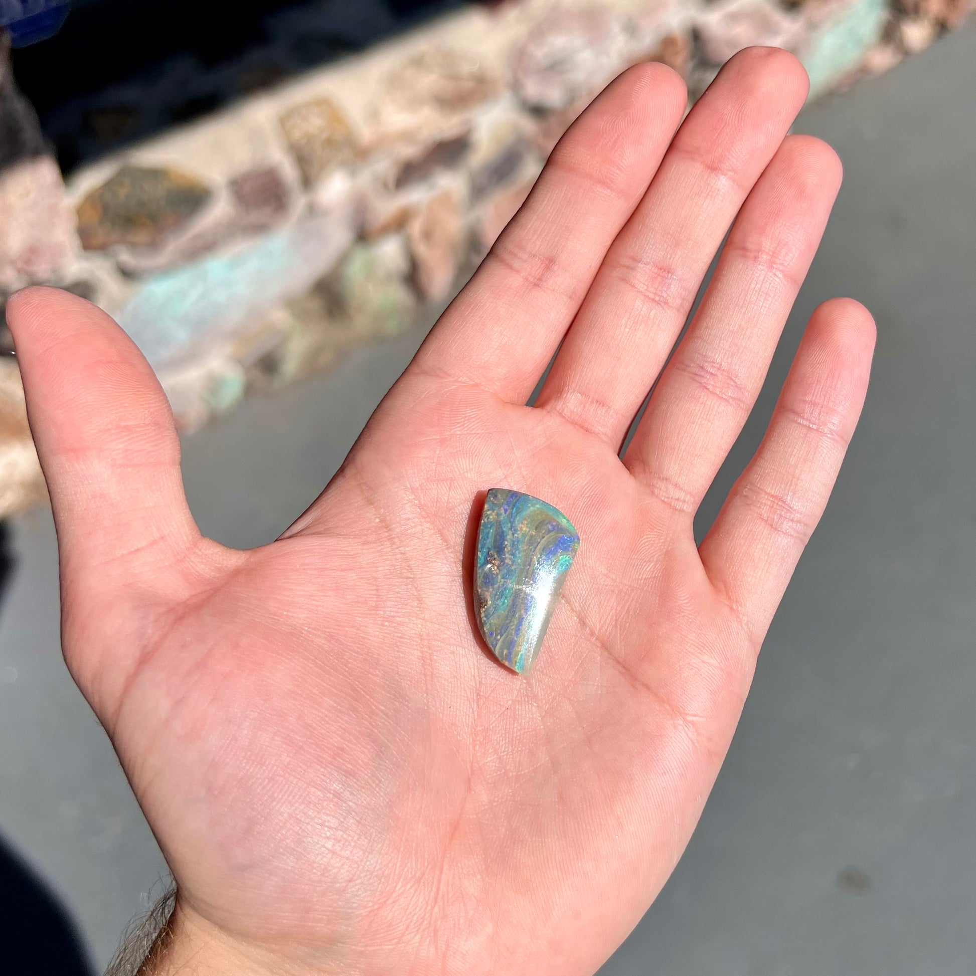 A polished, freeform shaped boulder opal stone from Queensland, Australia.  Predominant colors are green, blue, and violet.